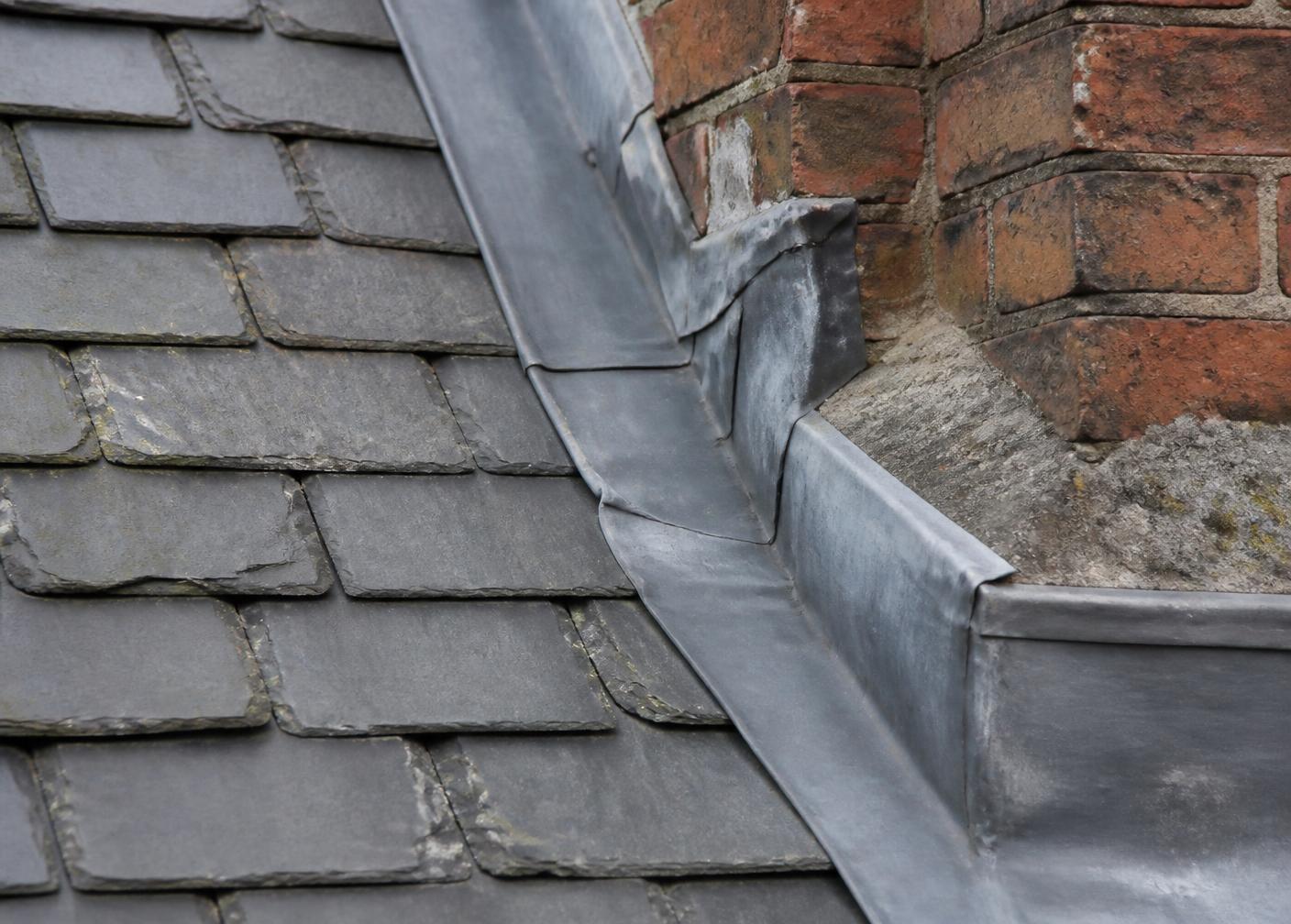 Close detail of slate tiles meeting lead flashing on a brick chimney